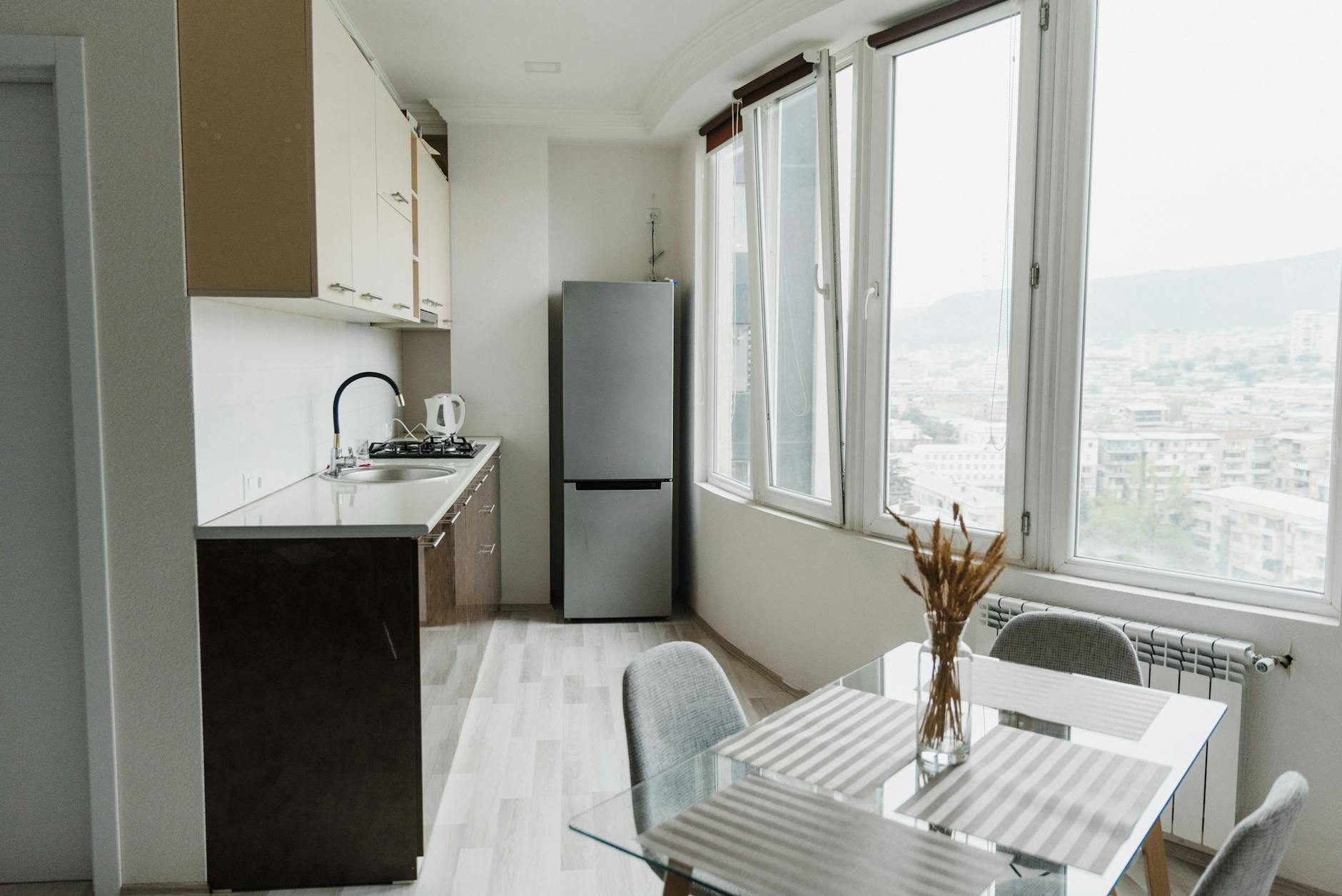 Meble kuchenne na wymiar czy gotowe zestawy – co wybrać do małego mieszkania Jasna nowoczesna kuchnia z przeszklonym stołem i widokiem na miasto