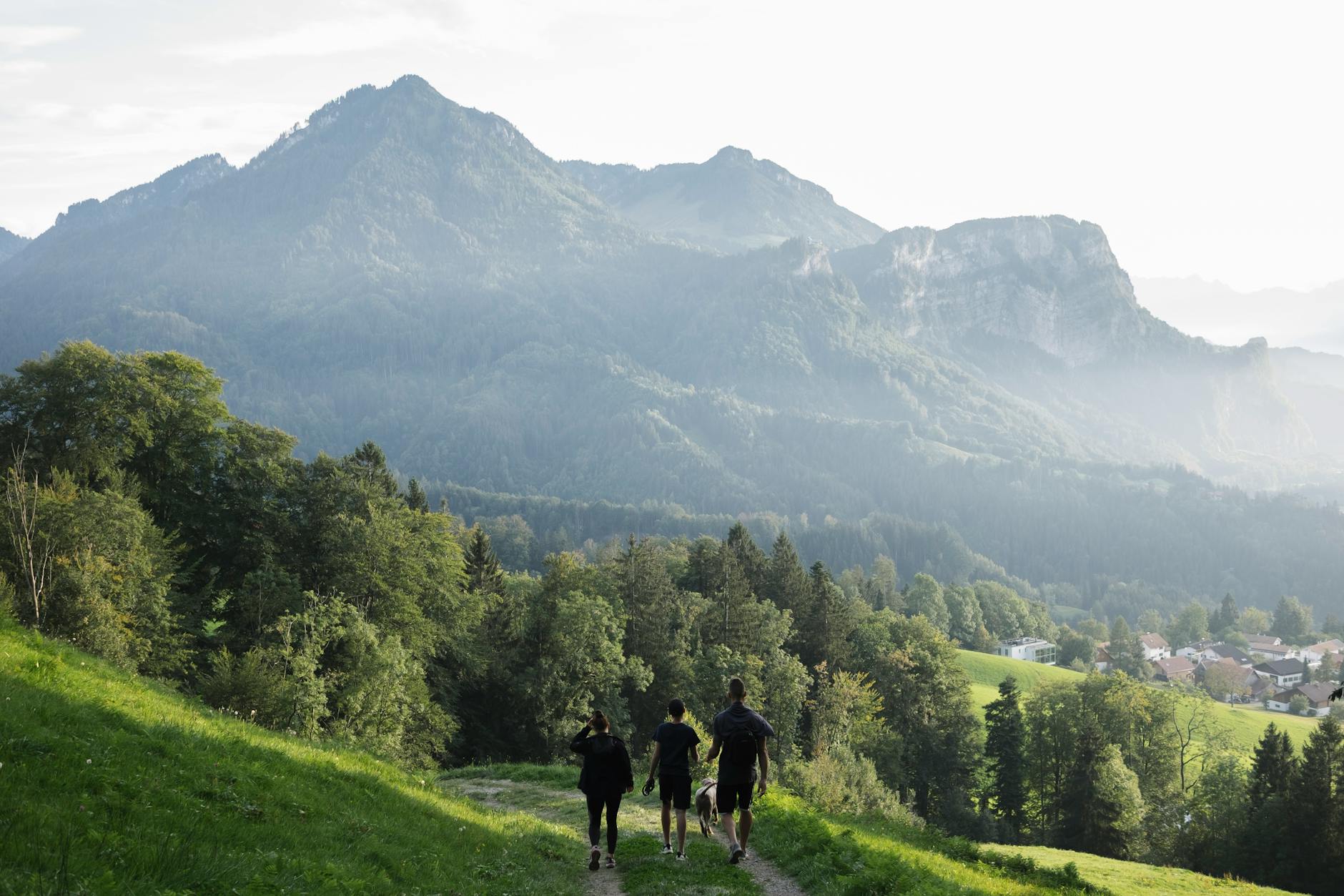 Turyści na górskim szlaku z widokiem na zielone stoki i wieś w dole